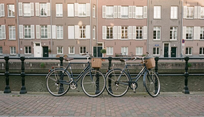 Two bicycles leaning on an iron canal railing over a cobbled Brussels quay, plain brick row houses with shutters in the background, soft morning light
